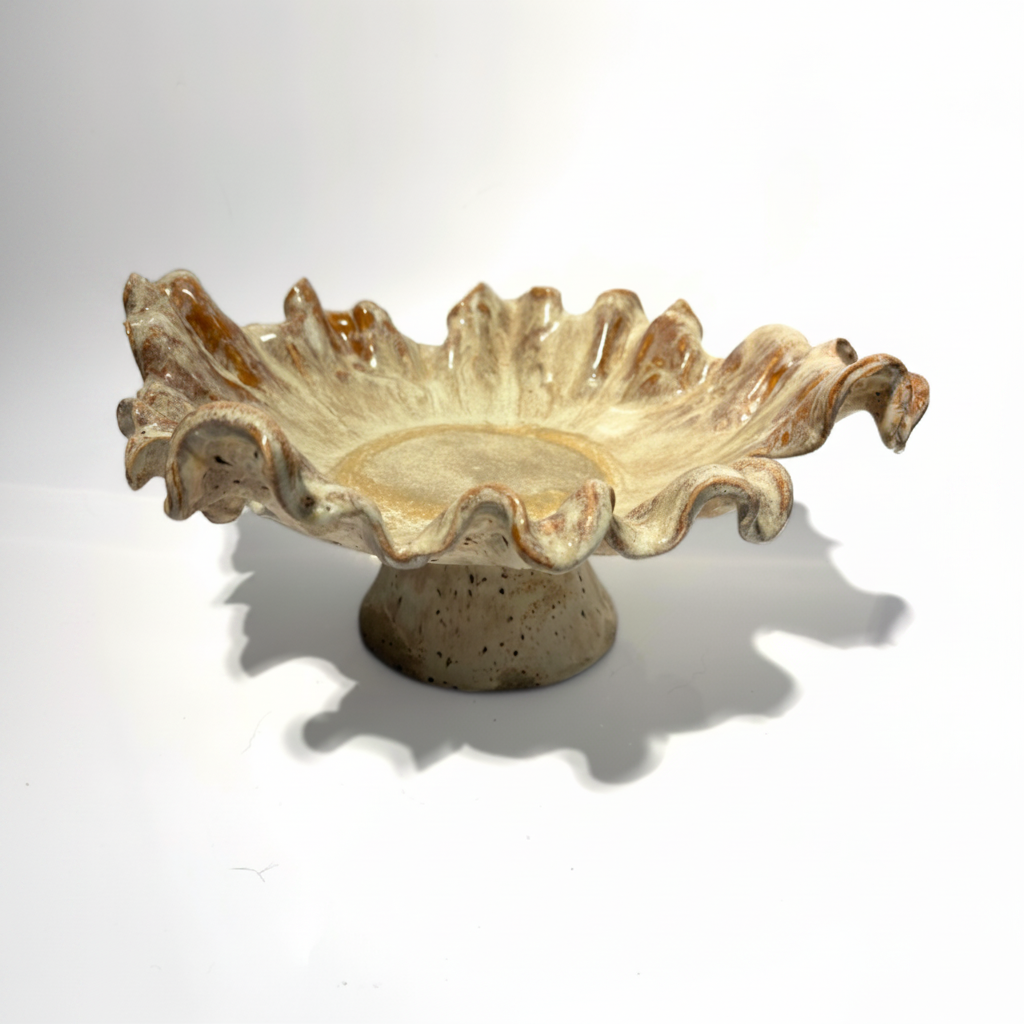 A decorative ceramic pedestal bowl with a ruffled, shell-like rim and a textured base, shown on a white background with a soft shadow.
